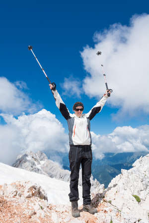 Young woman standing on top of a mountain with trekking poles raised highの写真素材
