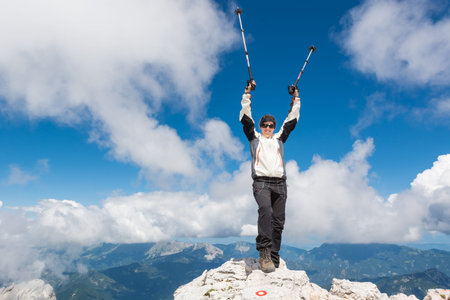 Female climber standing on top of a mountain and celebrating her successful ascend