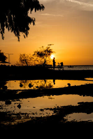 Silhouette of a cyclist standing on a beach. Reflection the ponds.の写真素材
