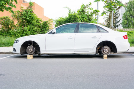 Car with stolen wheels. White vehicle left on wooden bricks.