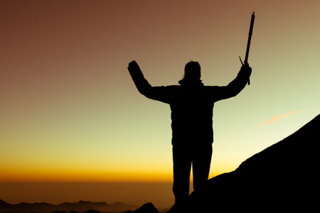 Silhouette of alpinist celebrating. Person holding ice axe at sunrise.