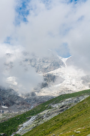 Mountain peak covered with clouds with glacier breaking under neath it.の写真素材