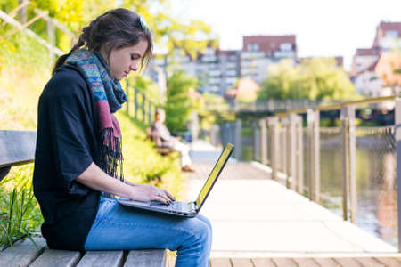 Young woman using laptop at a riverbank. Milleanial working in a park.の写真素材