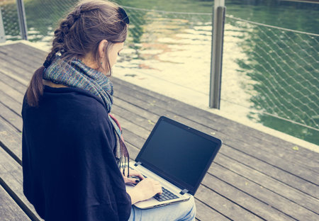 Young woman using laptop at a riverbank. Milleanial working in a park.の写真素材