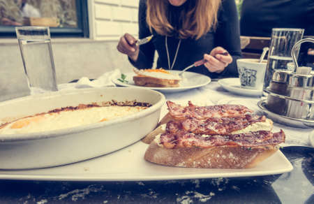 Young woman eating breakfast. Delicious fried bacon on crunchy toast with eggs from the oven.の写真素材