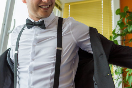 Groom wearing suspenders suiting up. Final wedding preparations.