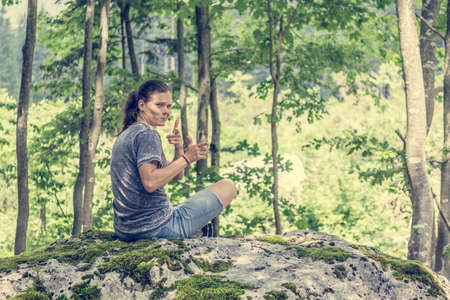 Young woman looking across her shoulder on a forest rock.の写真素材