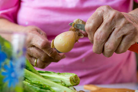 Closeup of elderly hands peaing potatoe.の写真素材