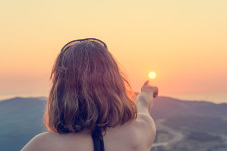 Attractive brunette pointing towards setting sun.