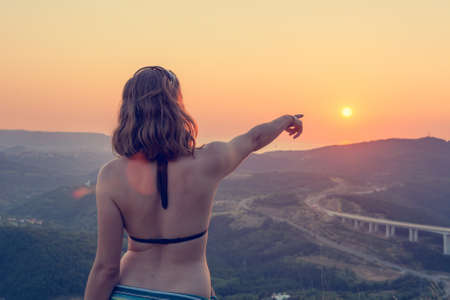 Attractive brunette pointing towards setting sun.の写真素材