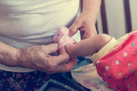 Closeup of elderly hands putting socks on newborn feet.