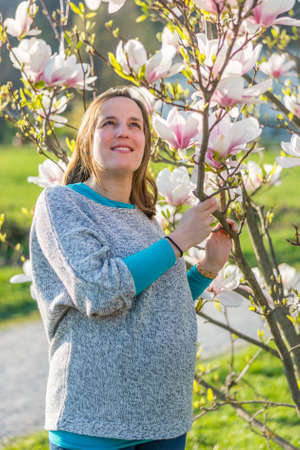 Pregnant woman posing by blooming magnolia tree.の写真素材