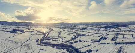 Aerial view of river flowing through snow covered countryside at sunset.の写真素材