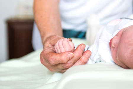 Closeup of newborn baby holding elderly hands.の写真素材
