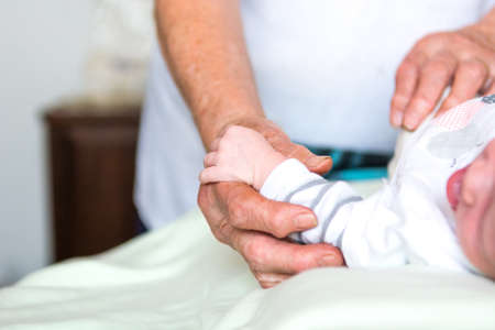 Closeup of newborn baby holding elderly hands.の写真素材