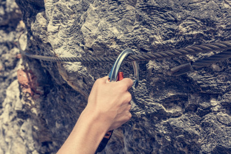 Closeup of female climber attaching via ferrata set to steel cable.