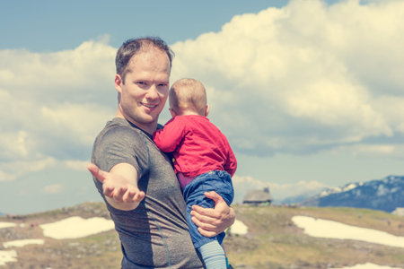 Young father holding his child in arms and inviting you to join.