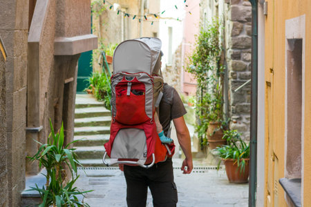 Father carrying his child in a carrier walking down narrow village street.