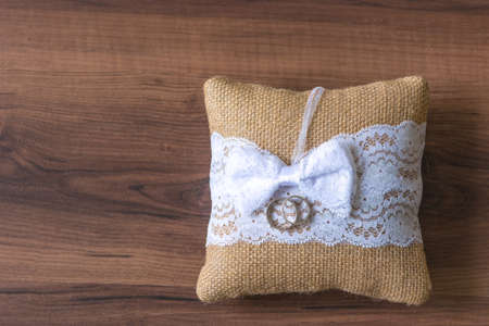 Vintage looking pillow with wedding rings on wooden desk.の写真素材