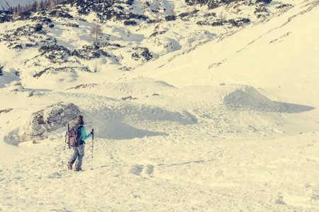Female alpinist descending into mountain valley crossing flakes of snow.