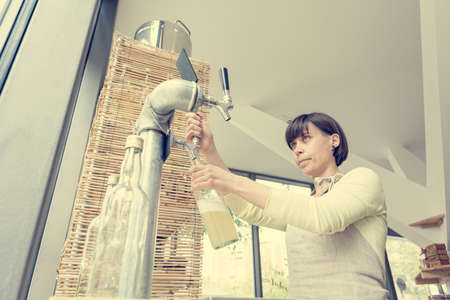 Young shopkeeper pouring delicious organic juice into glass bottle at zero waste store.の写真素材