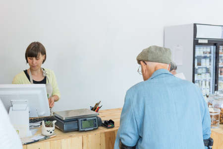 Elderly couple at cashier desk paying to teller in local zero waste store.の写真素材