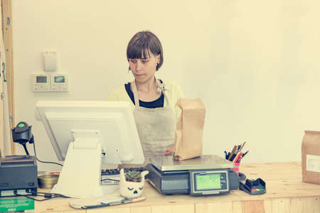 Young female shopkeeper at cash desk weighing food.の写真素材