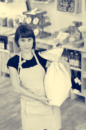 Happy female shopkeeper holding a flour bag in her arms.の写真素材