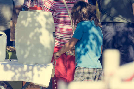 Rear view of child pouring a glass of water from plastic tank.の写真素材