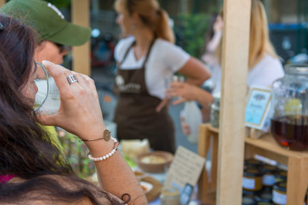 Rear view of female customer drinking at outdoor market place. Tasting delicious products.