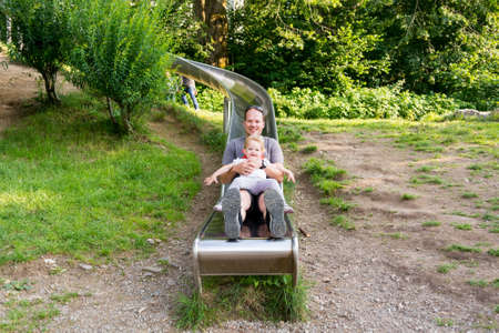 Father and daughter riding a long slide at local park.の写真素材