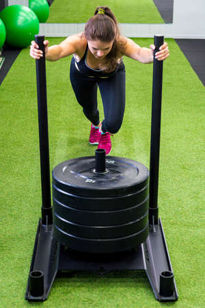 Young female fitness trainer performing sled push in local gym.の写真素材