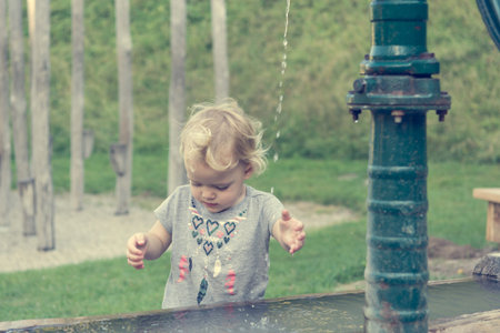 Cute blonde girl washing hands using hand water pump in local park.の写真素材
