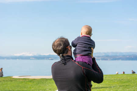 Rear view of a father holding his cute baby daughter and looking the sea.の写真素材