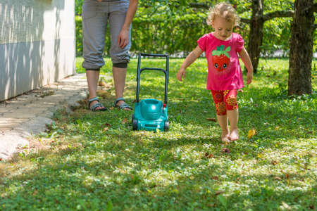 Cute girl lawn mowing with plastic toy mower.の写真素材