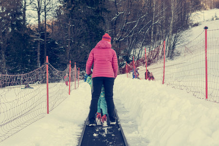 Rear view of mother helping her child on cki conveyor belt.