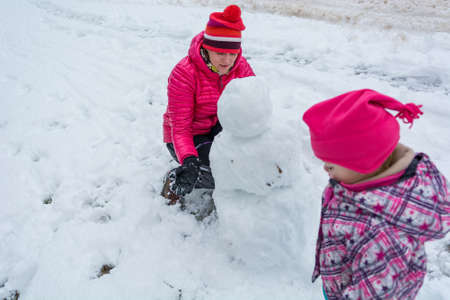 Mother and daughter building a snow outside enjoying the winter.の写真素材