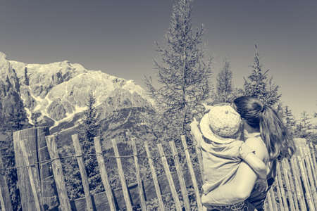 Mother holding her daughter in lap enjoying the mountain view and showing the landscape.の写真素材
