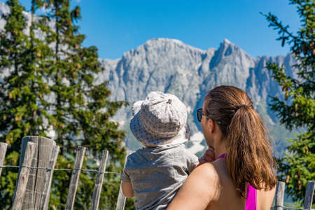 Mother holding her daughter in lap enjoying the mountain view and showing the landscape.の写真素材