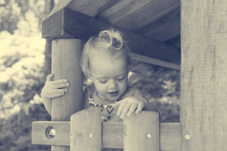 Cute blonde girl playing in wooden house looking through window.の写真素材