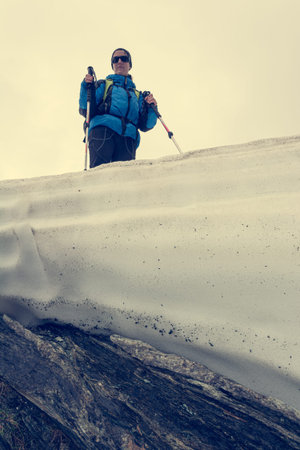 Female mountaineer standing on top of melting snow ridge.