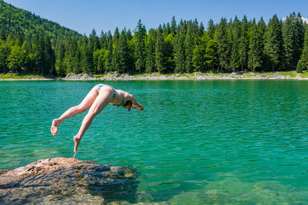 Attractive brunette jumping into crystal clean forest lake enjoying the summer. Lagho di Fusine, Italy.の写真素材