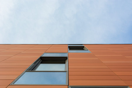Architecture detail of modern building with orange facade and windows reflecting the sky. Upwards...