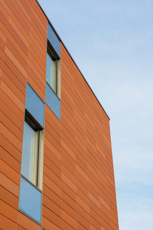 Architecture detail of modern building with orange facade and windows reflecting the sky. Upwards...