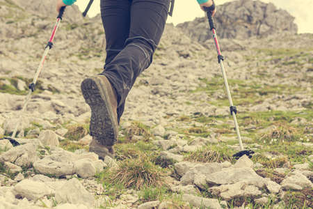 Low angle view of female ascending a rocky slope using walking poles.の写真素材