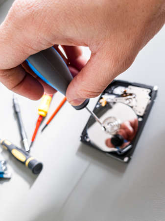 Repairing malfunctioned computer hard drive - removing screws and disassembling it. Repairman at work.の写真素材
