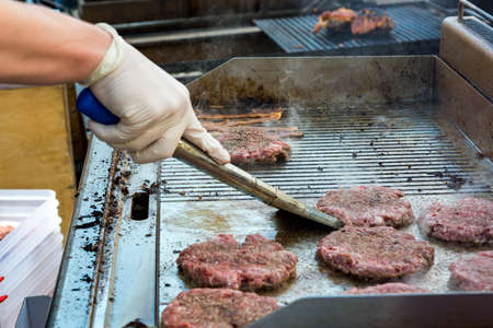 Chef preparing delicious burgers and flipping them on grill.の写真素材