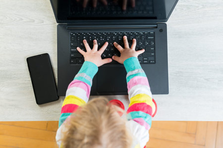 Drop down view of blonde girl programming on a computer while using mobile.