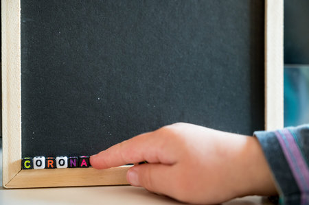 Child writing CORONA using alphabet beads on black board.