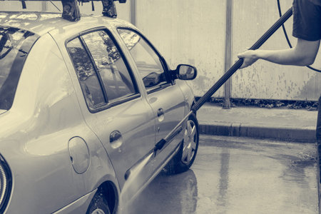 A man is washing a car at self service car wash. Detail of high pressure washer.